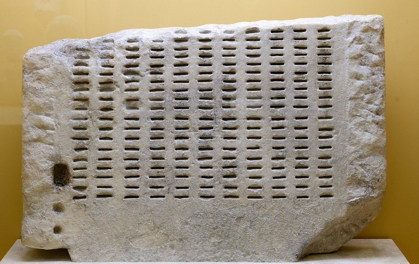 Fragmento de kleroterion, a máquina ateniense de sorteio de jurados, em mármore com fileiras de fendas